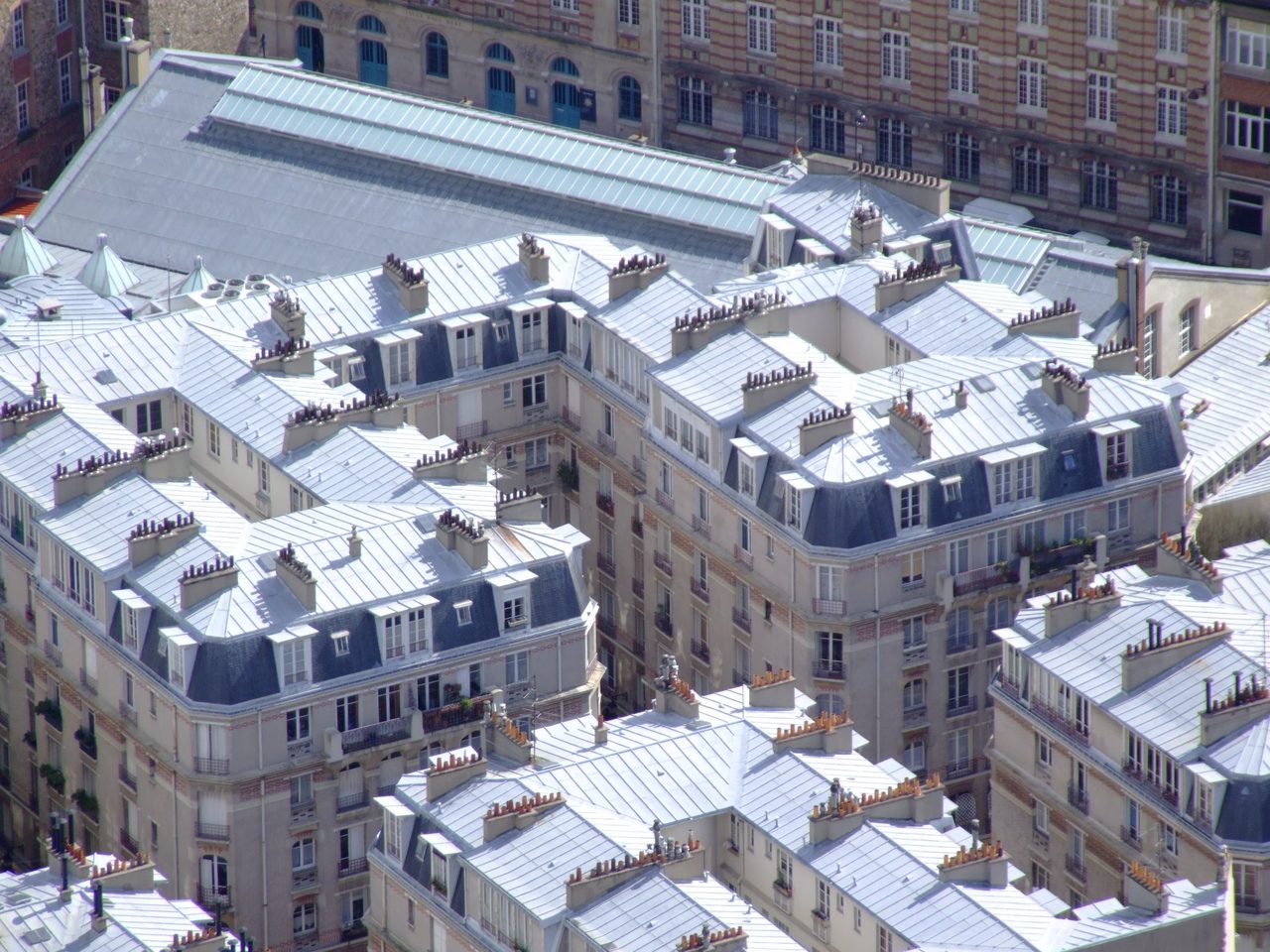 Vue aérienne des toits de zinc parisiens : mansardes, souches de cheminée et joints debout