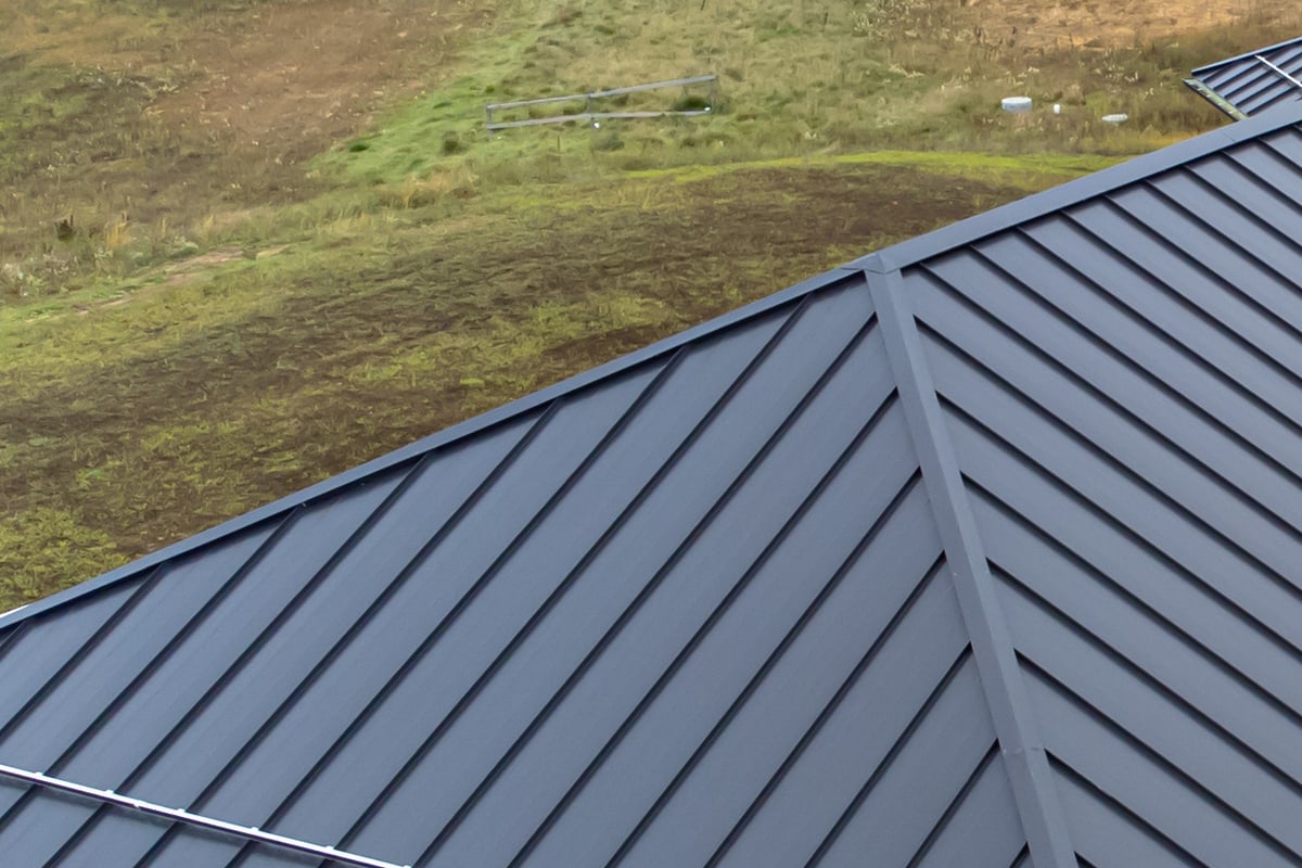Toiture en tôle d'acier à joint debout gris graphite : longues feuilles serties se rejoignant sur un arêtier